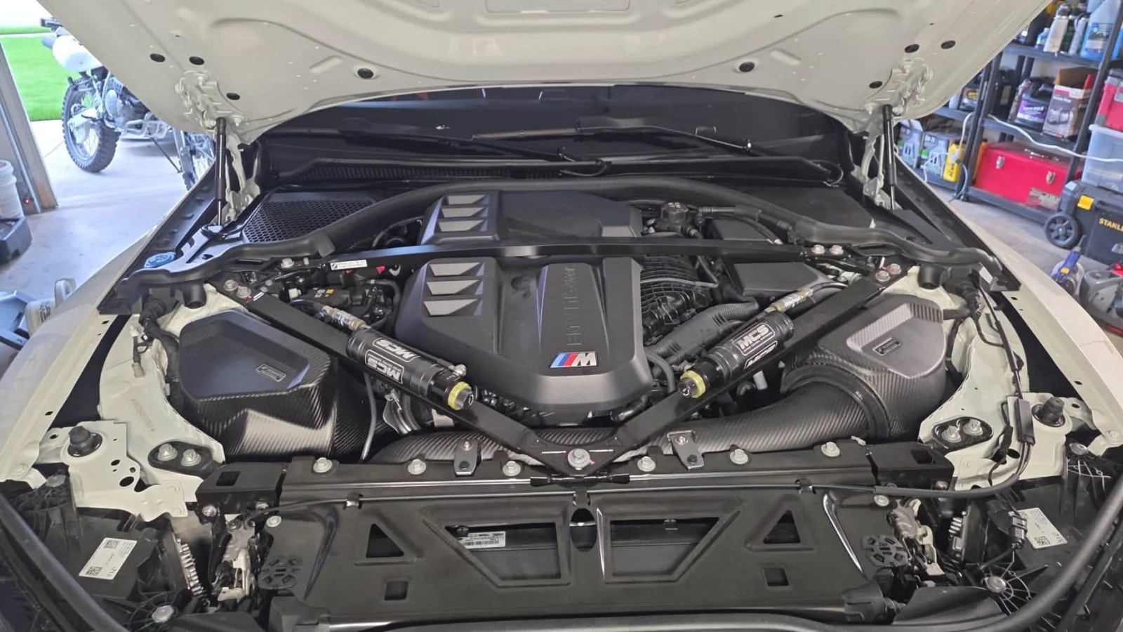 Engine bay of the M4 showing the S58 engine, MCS front dampers and carbon intakes
