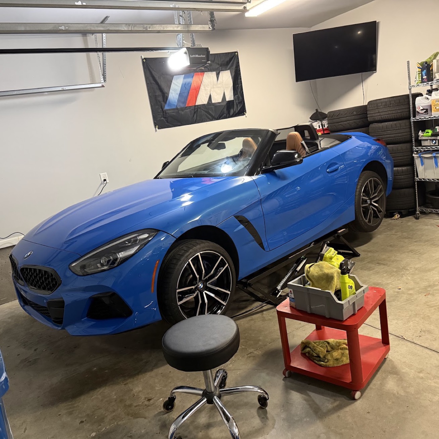 The G29 in the garage under the M banner, with the track tire stack on the shelf